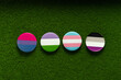 Bisexual, genderqueer, transgender, asexual badges on a green lawn grass.