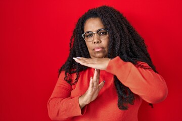 Poster - Plus size hispanic woman standing over red background doing time out gesture with hands, frustrated and serious face