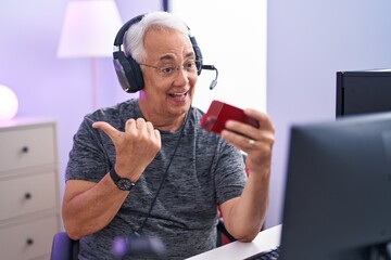 Poster - Middle age man with grey hair playing video games with smartphone pointing thumb up to the side smiling happy with open mouth