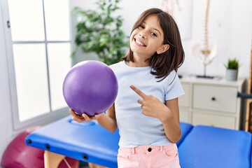 Sticker - Young hispanic girl holding small rehabilitation ball smiling happy pointing with hand and finger