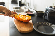 Hands Of Woman Cutting Orange Fruit With Knife In Kitchen At Home