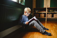Boy Reading Book Sitting On Floor At Home