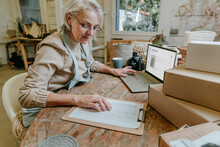 Craftswoman Reading Checklist Sitting With Laptop On Workbench