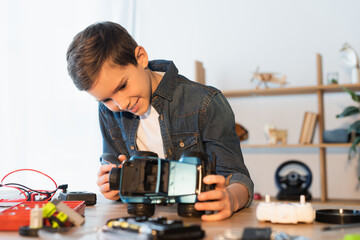 Canvas Print - happy boy holding handmade car model near blurred parts on table.