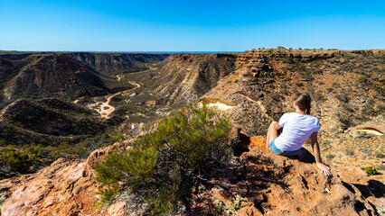 a long-haired girl sits on the edge of a gorge in cape range national park near exmouth in western a