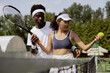 © ABCreative - Girl with Asian appearance came to first tennis lesson. Coach, guy with African appearance, teaches how to properly hold racket in hand. Girl has glasses and tennis cap on head.