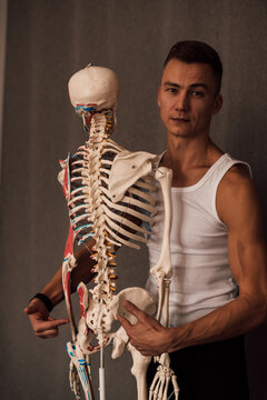 A man in a white T-shirt studies the structure of the human skeleton
