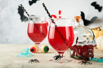 Halloween bloody cocktails. Two bloody cocktails glass goblets for Halloween and bottle form skull on light backgrounds. Decor concept for Halloween party with candy eyes, bats, spiders and pumpkins.