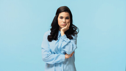 Wall Mural - skeptical young woman in shirt standing and looking at camera isolated on blue