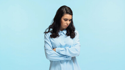 Wall Mural - sad young woman in shirt standing with crossed arms isolated on blue