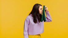 Brunette Woman In Purple Sweatshirt Smelling Stinky Socks Isolated On Yellow