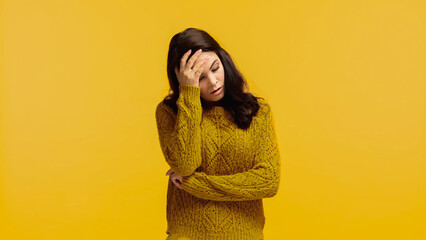 Wall Mural - upset and brunette woman in sweater touching forehead isolated on yellow