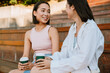 © Drobot Dean - Two asian women talking and drinking coffee while sitting on bench