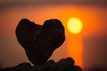 Wall Mural - Sea stone in the shape of a heart against with sunset