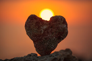 Wall Mural - Sea stone in the shape of a heart against with sunset