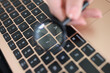 Female hand holding magnifying glass above laptop keyboard