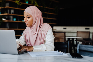 Wall Mural - Young muslim woman wearing headscarf smiling while working in office