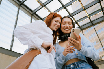 Wall Mural - Young multinational women smiling and using cellphone indoors