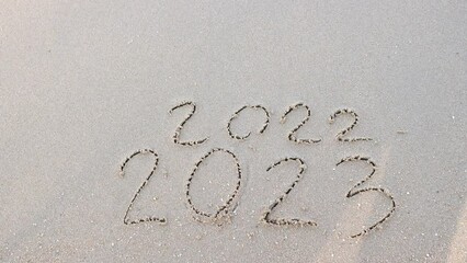 Wall Mural - message year 2022 replaced by 2023 written on beach sand background. goodbye 2022 hello to 2023 lapp