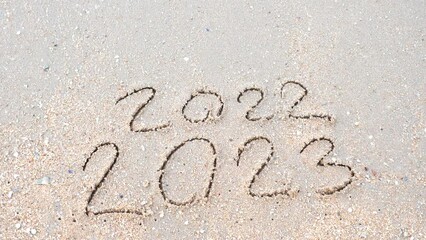 Wall Mural - message year 2022 replaced by 2023 written on beach sand background. goodbye 2022 hello to 2023 lapp