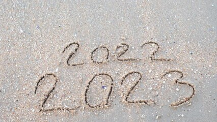 Wall Mural - message year 2022 replaced by 2023 written on beach sand background. goodbye 2022 hello to 2023 lapp