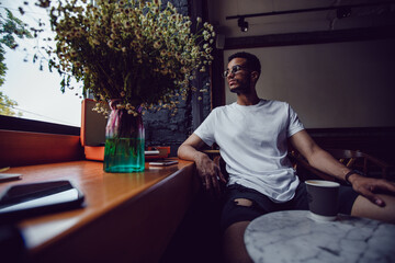 Wall Mural - African american man in a white t-shirt sits in a coffee shop and uses the phone. Mock-up.