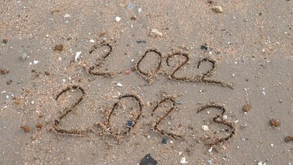 Wall Mural - message year 2022 replaced by 2023 written on beach sand background. goodbye 2022 hello to 2023 lapp