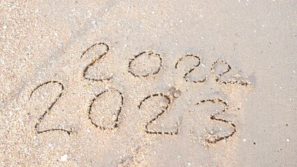 Wall Mural - message year 2022 replaced by 2023 written on beach sand background. goodbye 2022 hello to 2023 lapp