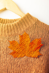 Wall Mural - Autumn concept. A maple leaf is attached to a brown chunky knit sweater, close-up. The sweater hangs on wooden coat hangers, fragment, close-up. Maple leaf with knitted sweater texture.