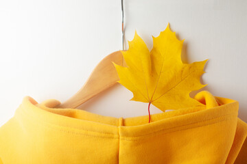 Wall Mural - Autumn concept - one autumn yellow maple leaf lies in the hood of a yellow sweatshirt that hangs on a hanger. Close-up