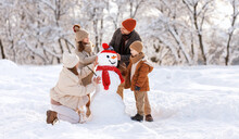 Happy Children Sculpting Funny Snowman Together With Parents In Winter Snow-covered Park