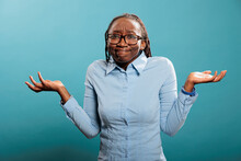 Puzzled And Doubtful Young Adult Person Being Hesitant And Unconfident While Answering Question. Confused And Uncertain Woman Shrugging Shoulders With Uncertainty While Standing On Blue Background.