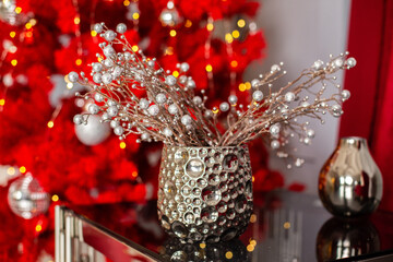 Wall Mural - Natural Christmas composition from decorative branches with beads in a vase on background of redchristmas tree. Christmas mood. Stylish composition