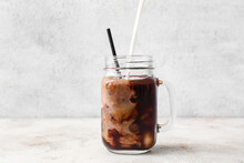 Pouring Of Milk Into Mason Jar With Delicious Iced Coffee On Light Background