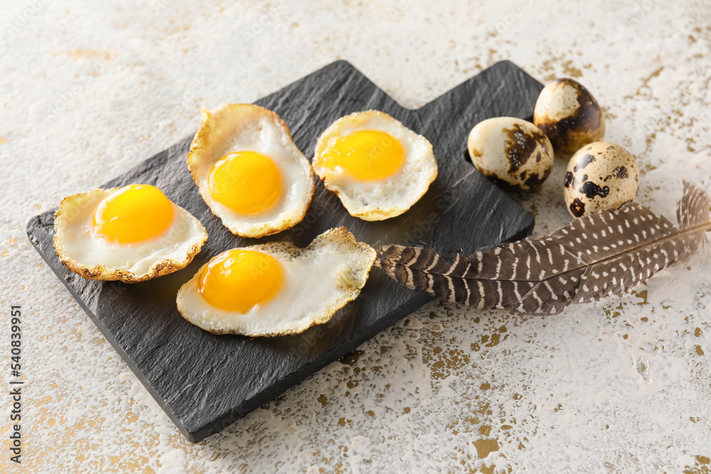 Slate board with fried quail eggs on light background, closeup
