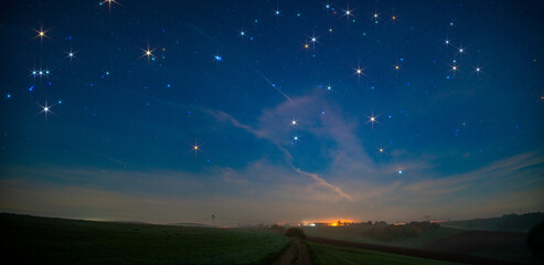 Wall Mural - panorama of a night field with a country road and a village On the horizon a starry sky