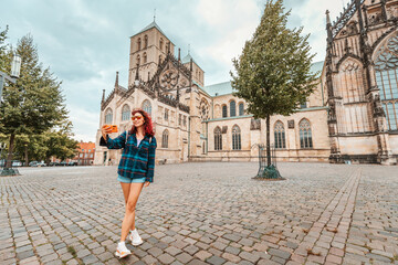 Wall Mural - Happy tourist girl taking selfie photo while visiting St. Paulus Dom Cathedral and admiring old town architecture buildings in Munster, Germany