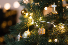 Golden Christmas Tree Toys On Green Branches Of A Christmas Tree. Garland Lights And Festive Atmosphere. Space For Text