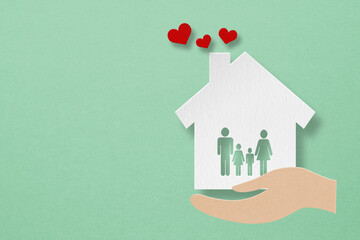 white house paper cut with family icon inside and red heart over hands on grunge green background including copy space