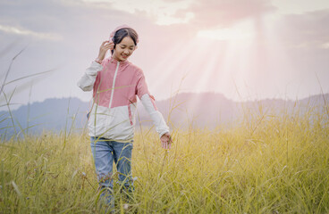 Poster - Young teenager girl enjoy listening to music with headphone with feeling happy and relaxed on mountain park sunset background