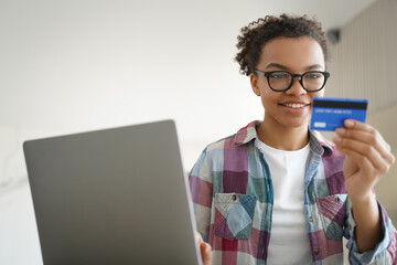 Mixed race teen girl holds credit card, using online banking services at laptop at home. E commerce