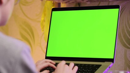 A girl is sitting at a laptop with a green screen and typing