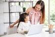 © aekkorn - Children education and home school concept : Young asian mother pleased to see little daughters' study online. Excited smiling child girl enjoying online learning  with pleasant mom at home.