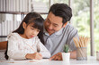 © aekkorn - Children education and home school concept : Young asisn father pleased to see little daughters' study success. Excited smiling small child girl enjoying learning and writing with pleasant dad at home
