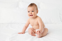 Cute Baby Sitting On White Bed Holding Foot