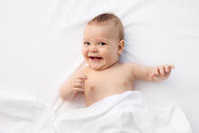 Joyful Baby Lying On White Bed Looking At Camera