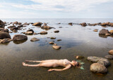naked woman lies in mud on the seashore.