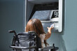 © Manuel - Disabled woman with reduced mobility and small stature in an electric wheelchair trying to withdraw money from an ATM. Concept handicap, disability, incapacity, special needs, architectural barriers.