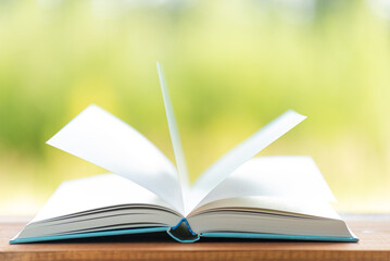 Wall Mural - Open book on wooden table on natural background. Concept of reading books. Wind turns the pages. Image with shallow depth of field.