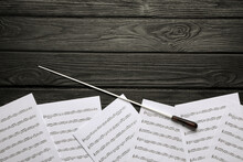 Conductor's Baton And Sheet Music On Black Wooden Table, Flat Lay. Space For Text